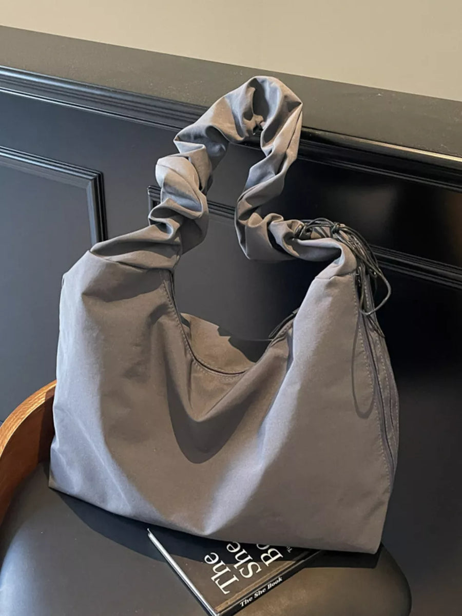 Gray ruched nylon shoulder bag with zipper and decorative tassels.