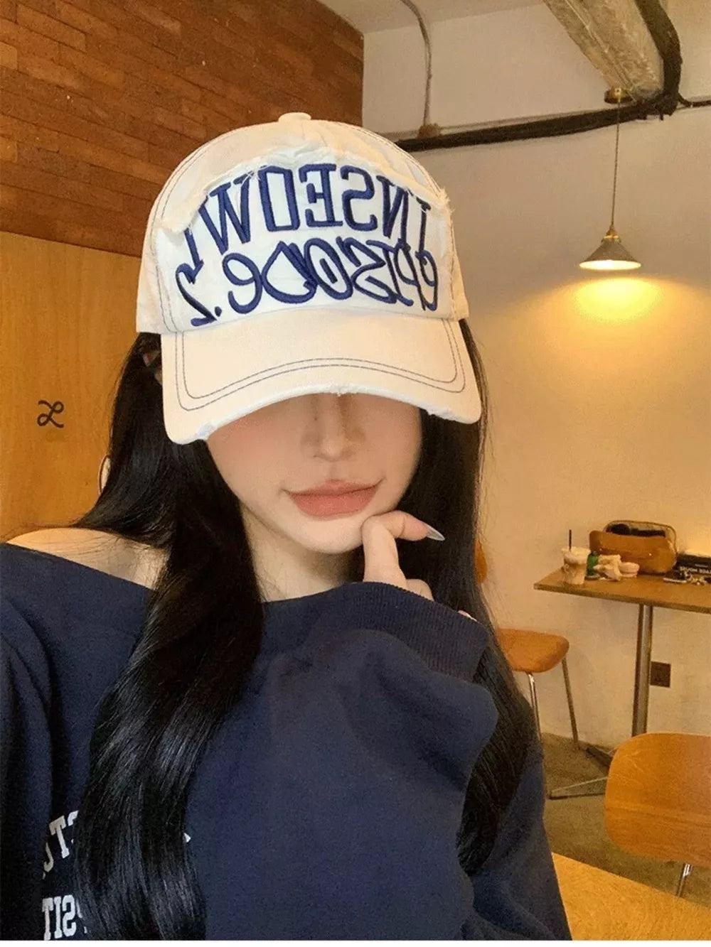 White distressed baseball cap with blue embroidered text and frayed details.