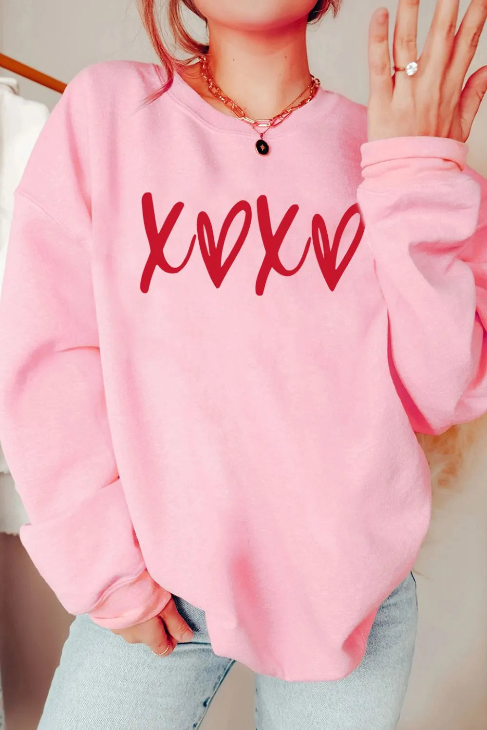Blush pink relaxed fit sweatshirt with red XOXO graphic print and crew neck.