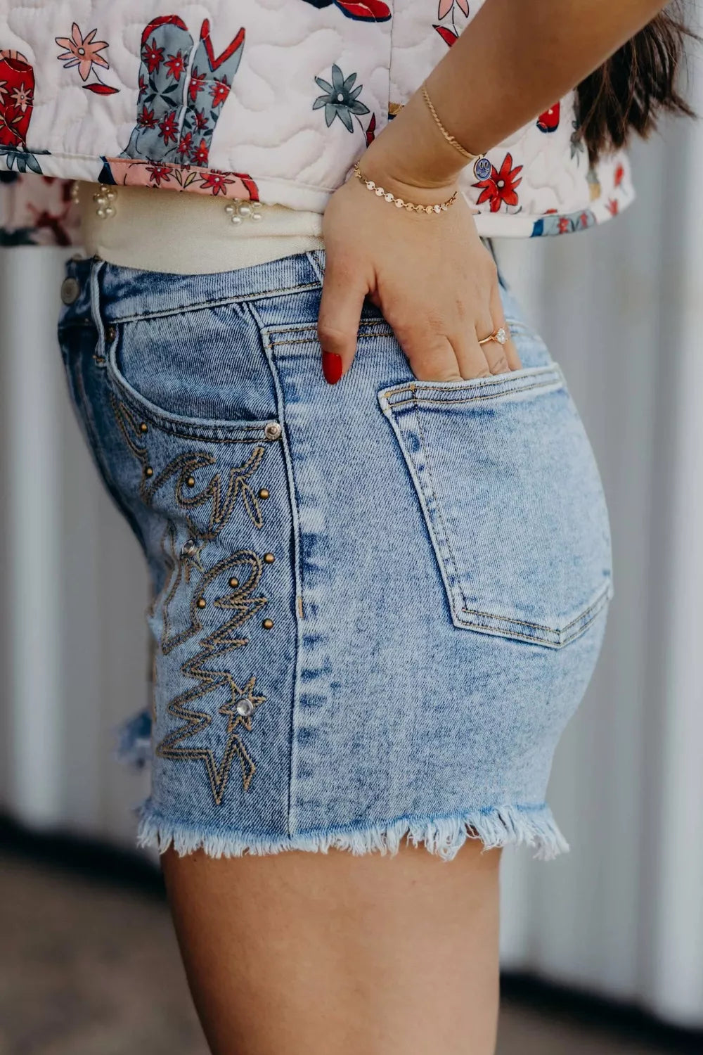 Light wash denim shorts with distressed frayed hem and embroidered western star details.