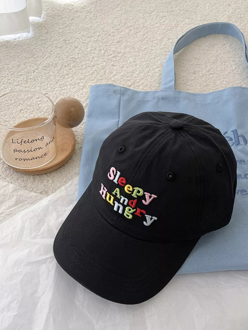 Black baseball cap with "Sleepy And Hungry" embroidered in colorful text.