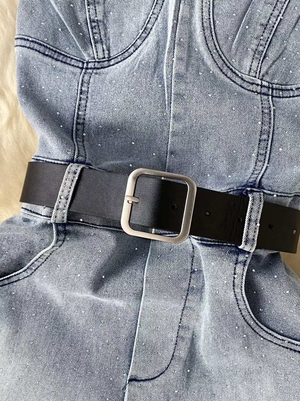 Blue denim romper with allover rhinestones and black belt with silver buckle.