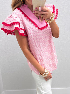 Pink eyelet embroidered blouse with flutter sleeves and red lace trim.