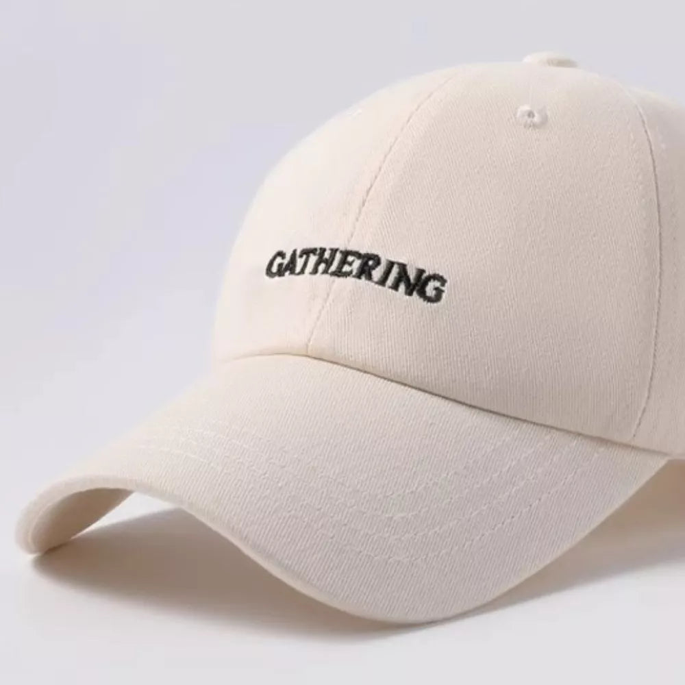Beige cotton baseball cap with embroidered "GATHERING" text detail.