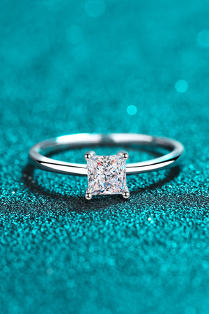 Silver ring with a square cut moissanite diamond on a sparkly blue background.