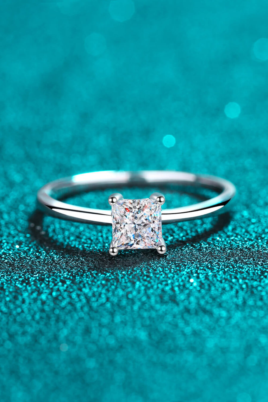 Silver ring with a square cut moissanite diamond on a sparkly blue background.