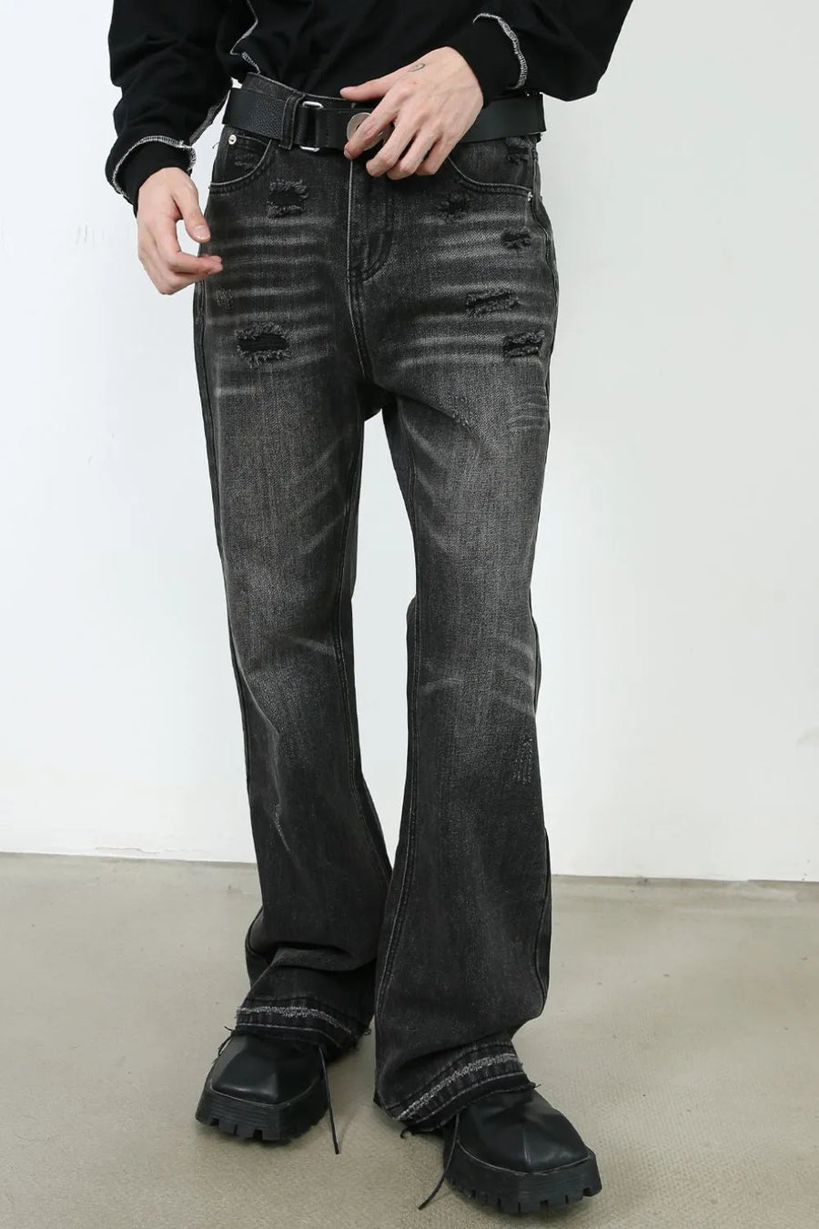 Distressed flare jeans in washed black denim with ripped details and a raw hem.