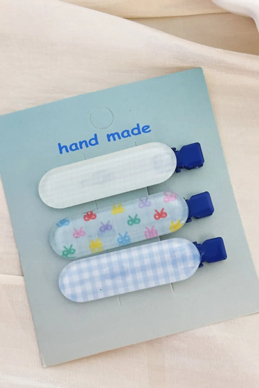 Pastel patterned hair clips trio with blue clasps, featuring gingham and bow designs.