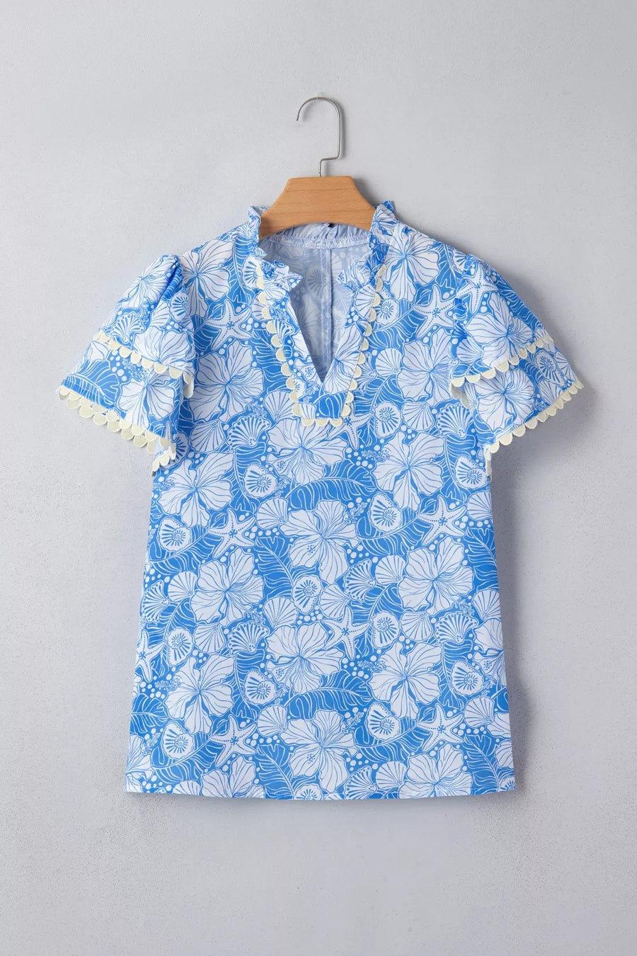Blue tropical floral print v-neck blouse with frill trim and short sleeves.