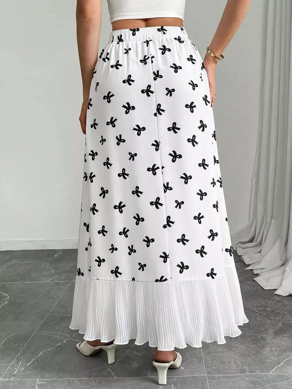 White maxi skirt with black bow print and pleated hem.