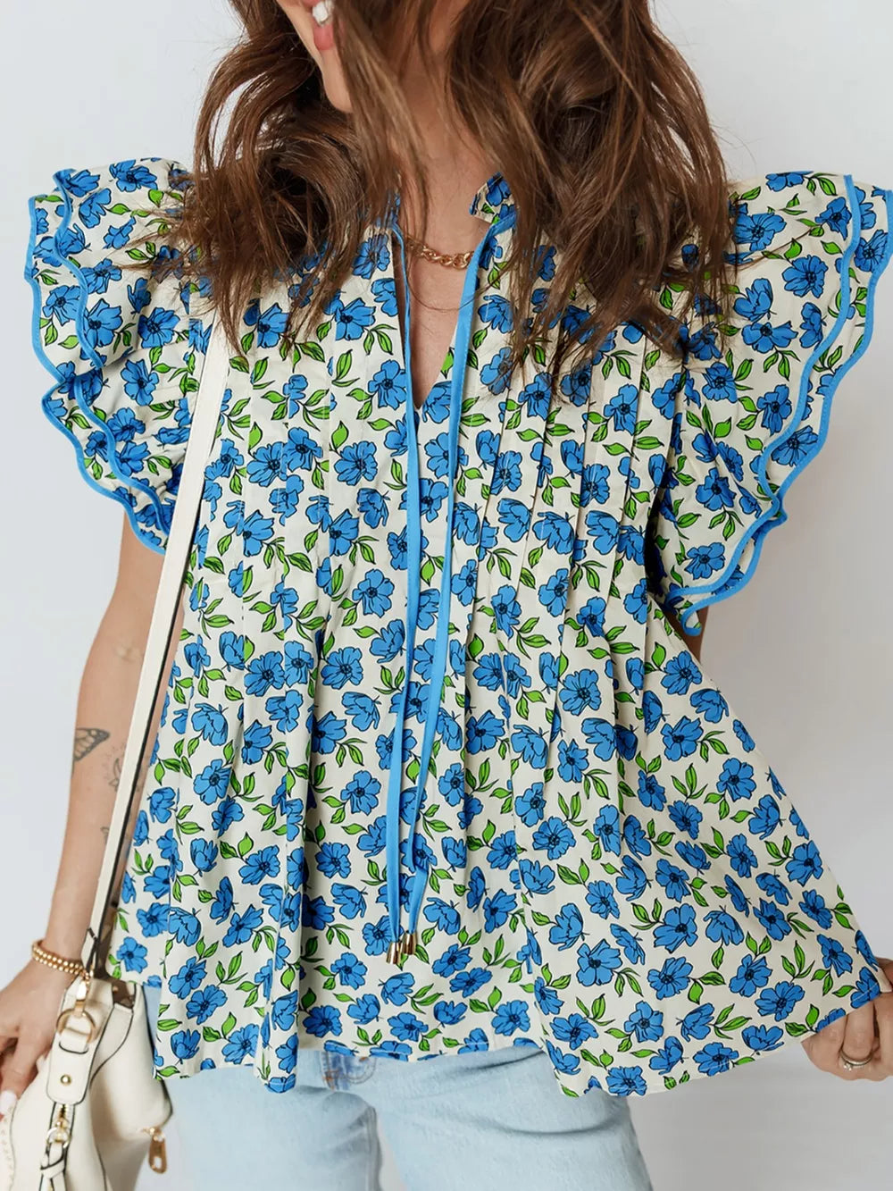 Floral ruffle sleeve tie-neck blouse with blue flowers and green leaves on a cream cotton fabric.