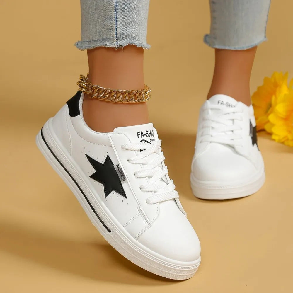 White sneakers with black star patches and laces, featuring a gold ankle chain.