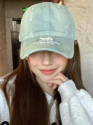 Distressed baseball cap in dirty blue cotton with white embroidery and frayed details.