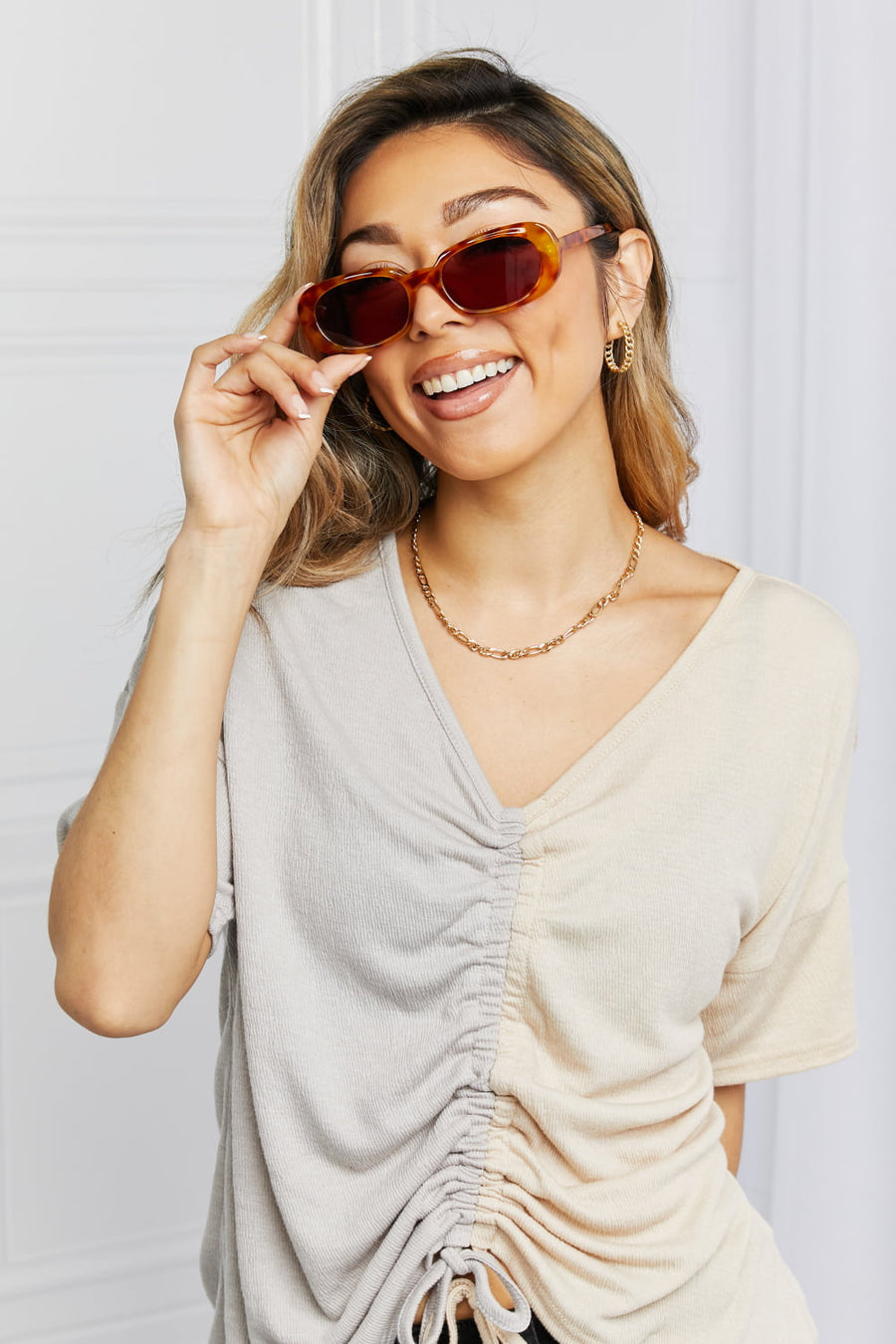 Tortoiseshell oval sunglasses with dark lenses, worn by a woman with a ruched two-tone top.