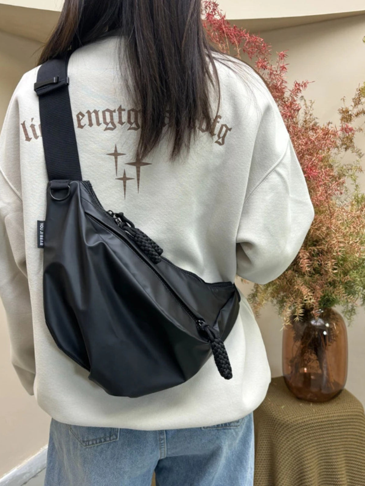 Black nylon crossbody bag with braided zipper pull detail worn by a woman.