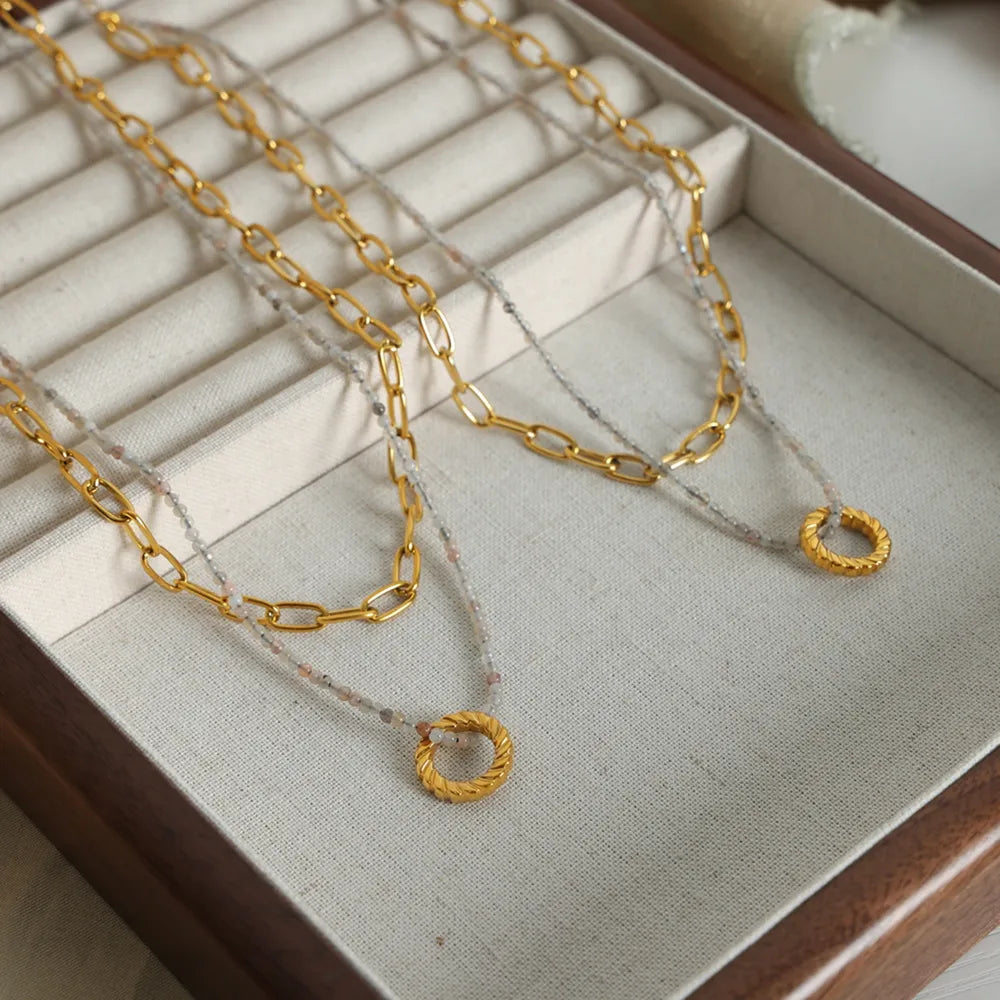 Gold layered chain necklace with beaded strand and twisted circle pendant.