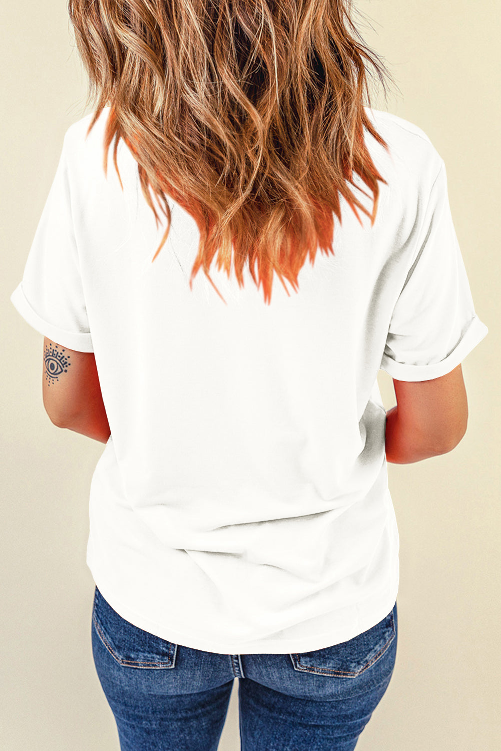 White t-shirt with cuffed short sleeves and a subtle eye tattoo on the arm.