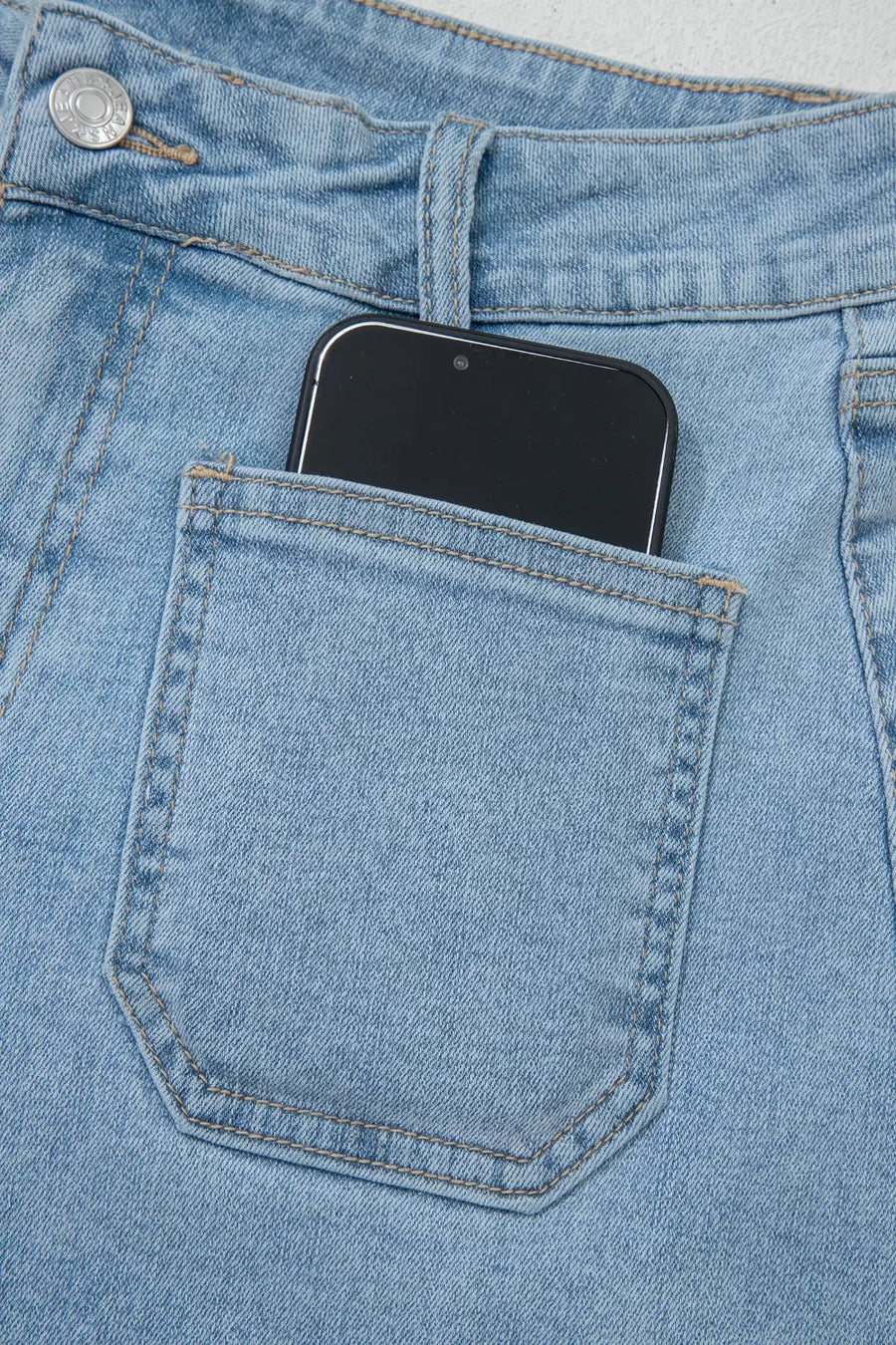 Light wash denim shorts with patch pocket detail, showing a smartphone.