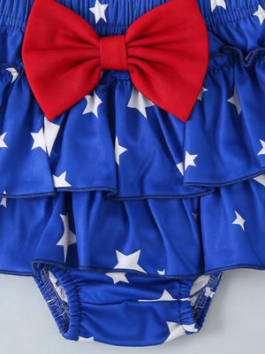 Royal blue baby outfit with white stars, tiered ruffles, and a red bow.