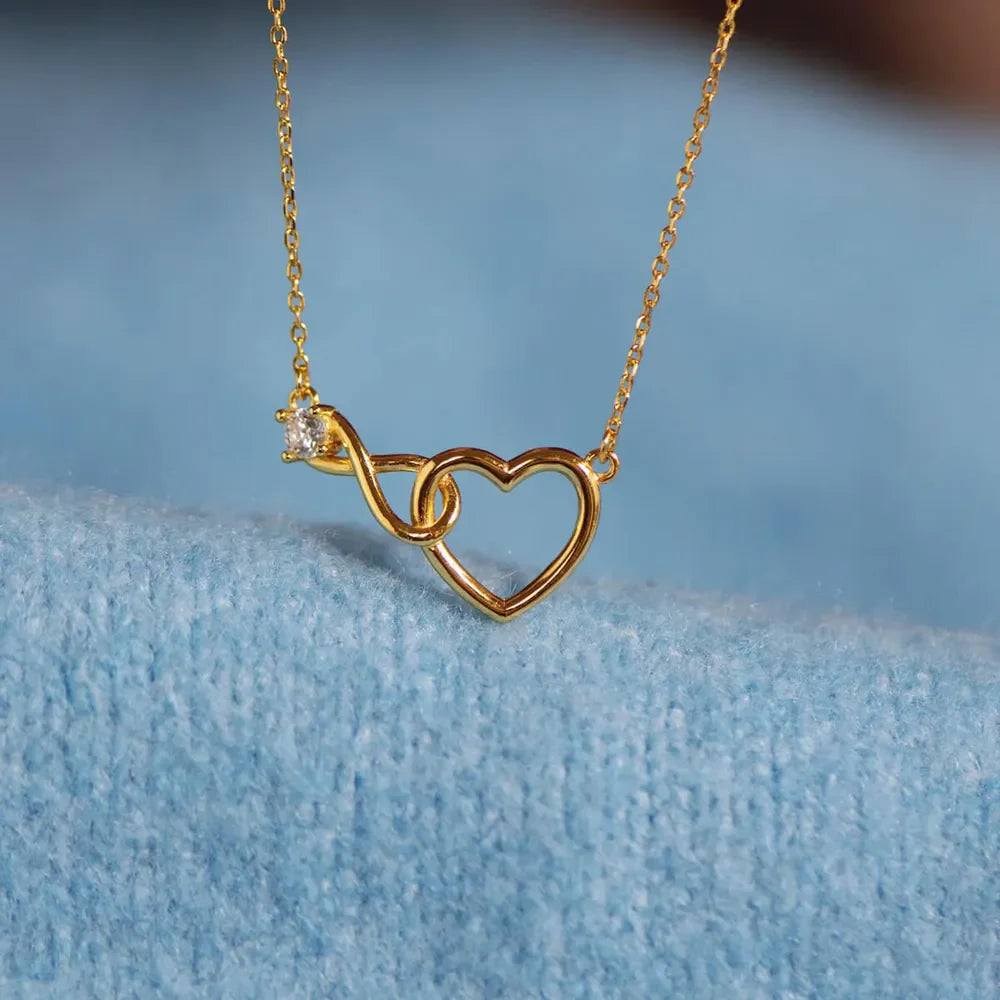 Gold necklace with intertwined heart and infinity symbol pendant featuring a cubic zirconia accent.