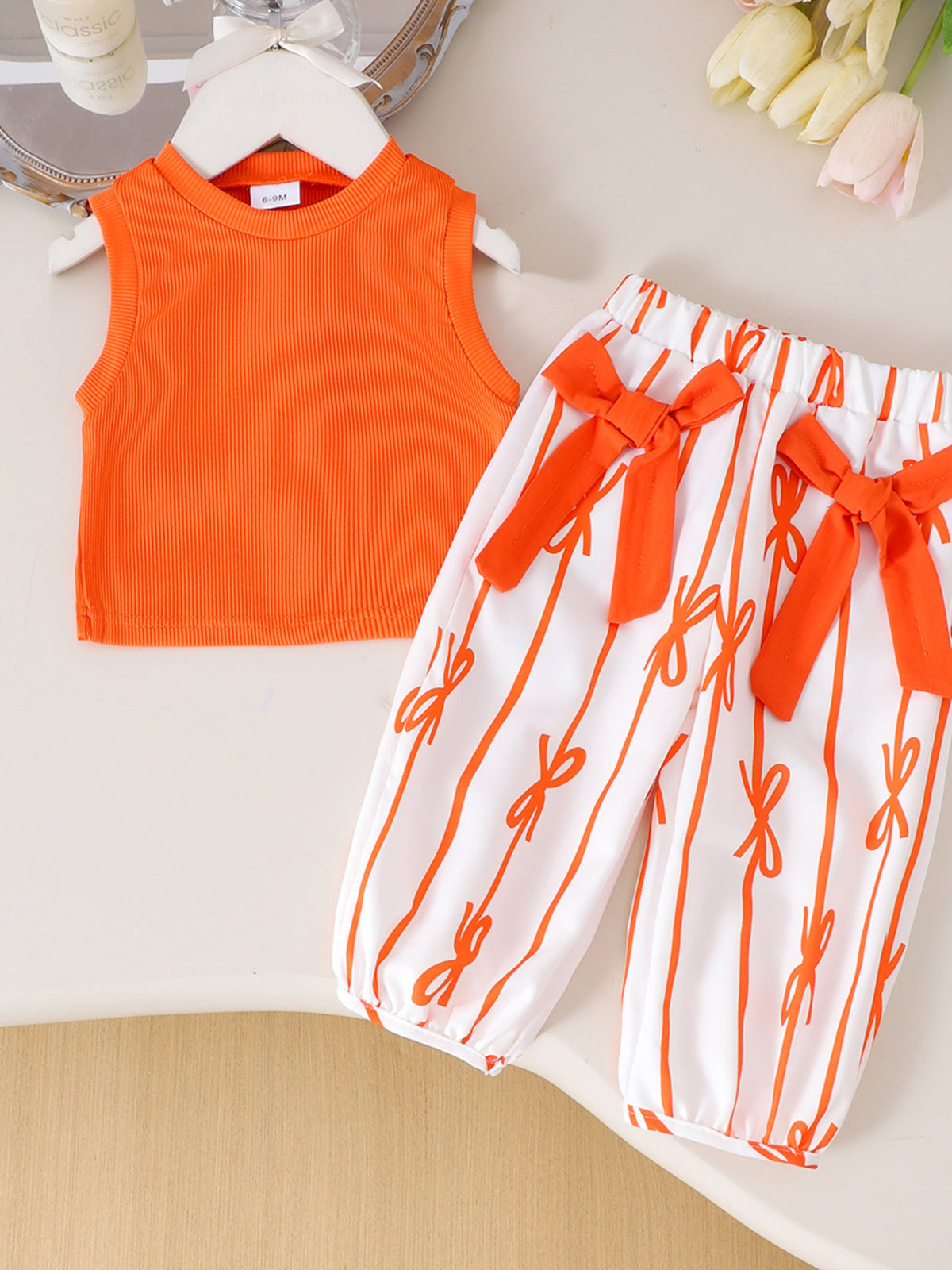 Orange ribbed tank top and white striped pants with orange bows for baby girls.