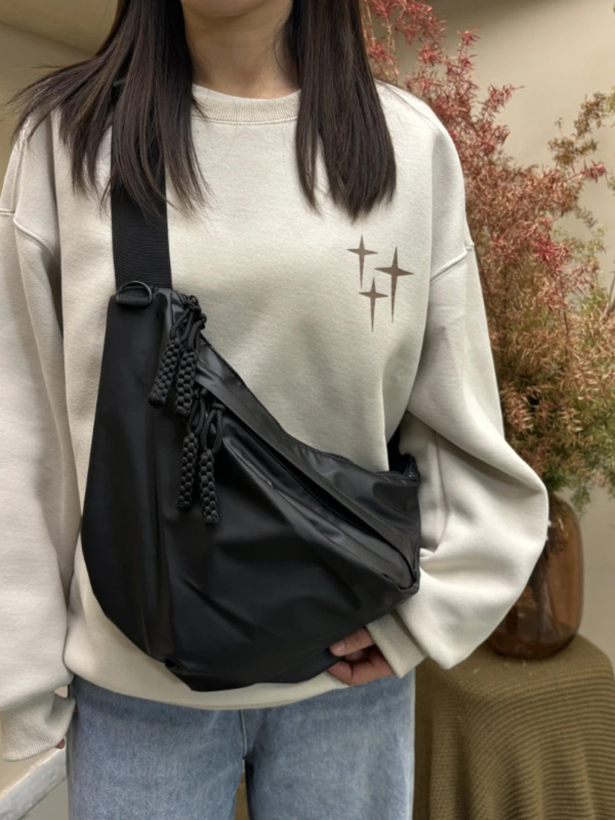 Black nylon crossbody bag with braided tassel details and a single strap.