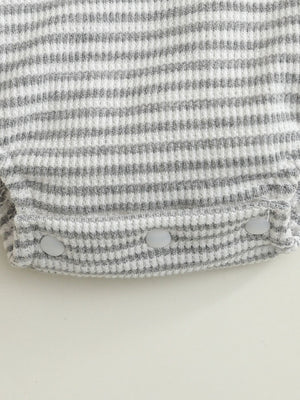 Baby one-piece with grey and white stripes, waffle knit, and snap closures.