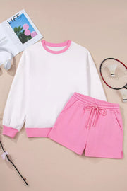 White crewneck sweatshirt with pink trim and pink drawstring shorts.