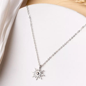 Silver sunburst pendant necklace with lace trim detail on a delicate chain.