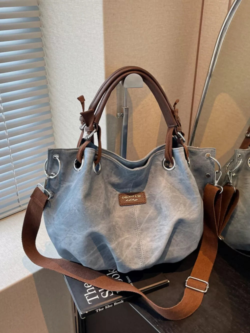 Blue slouchy crossbody bag with brown leather straps and adjustable canvas strap.
