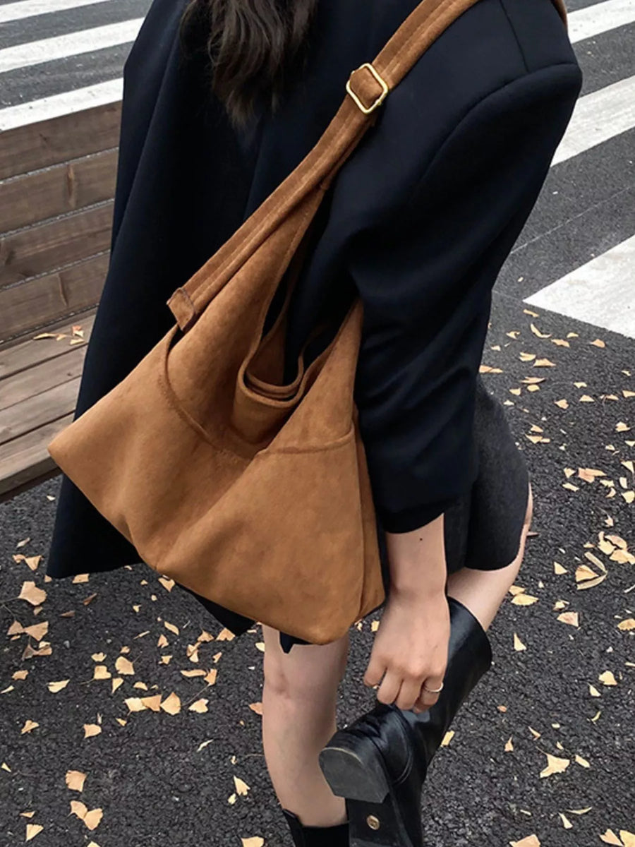 Large brown suede shoulder bag with gold buckle detail, worn by a woman.