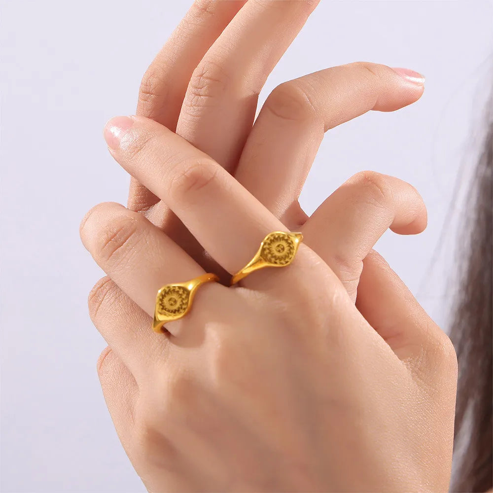 Gold sunburst signet rings with intricate pattern detail on a hand.