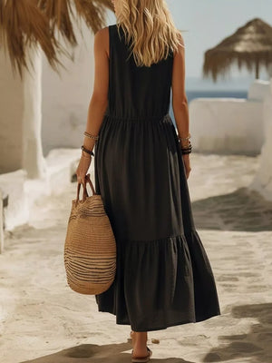 Black sleeveless maxi dress with ruffled hem and cinched waist, worn with a straw bag.