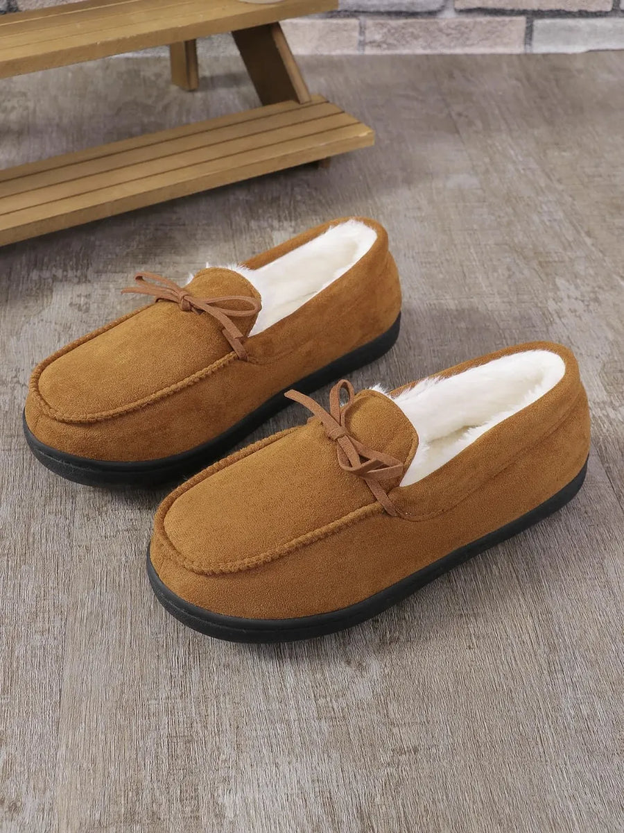 Caramel suede moccasin slippers with white faux fur lining and bow detail.