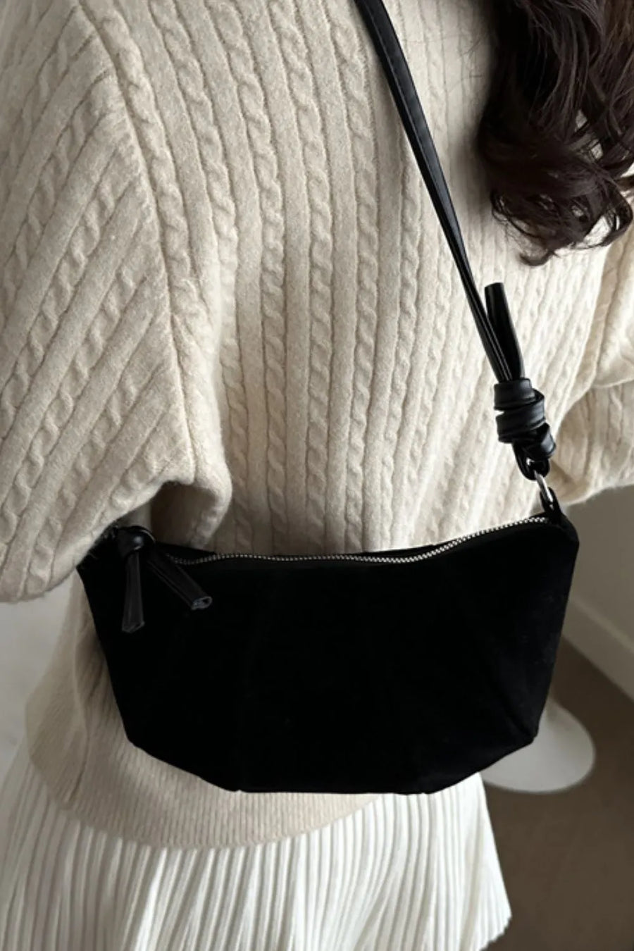 Black suede crescent shoulder bag with pleated detail and knotted strap.