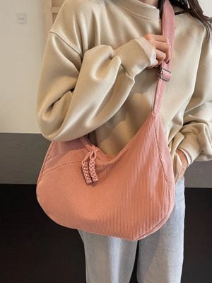 Pink corduroy crescent shoulder bag with braided zipper pull detail