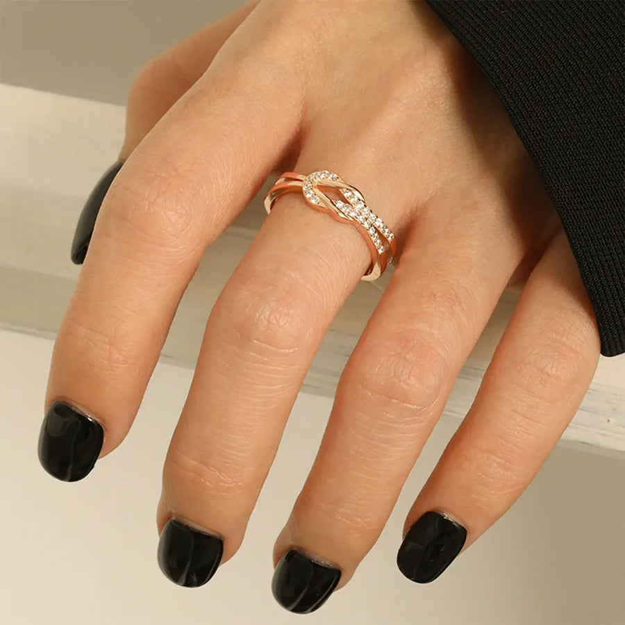 Rose gold knot ring with pave zirconia detail on a hand with black nails.