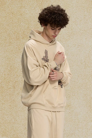 Khaki relaxed fit hoodie with embroidered bird graphic on chest and sleeve.
