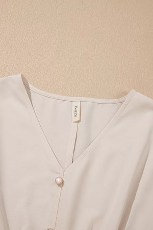Elegant v-neck polyester blouse in cream with decorative pearl buttons.