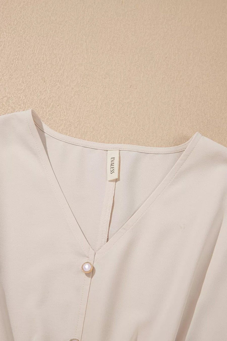 Elegant v-neck polyester blouse in cream with decorative pearl buttons.