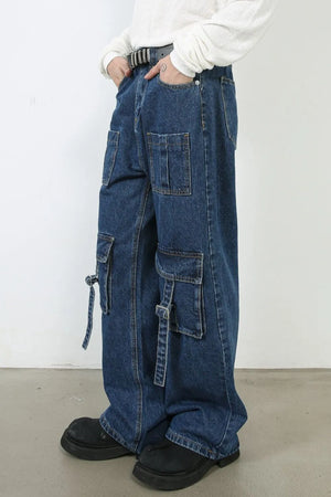 Medium wash denim cargo pants with buckle strap pockets and wide leg cut.