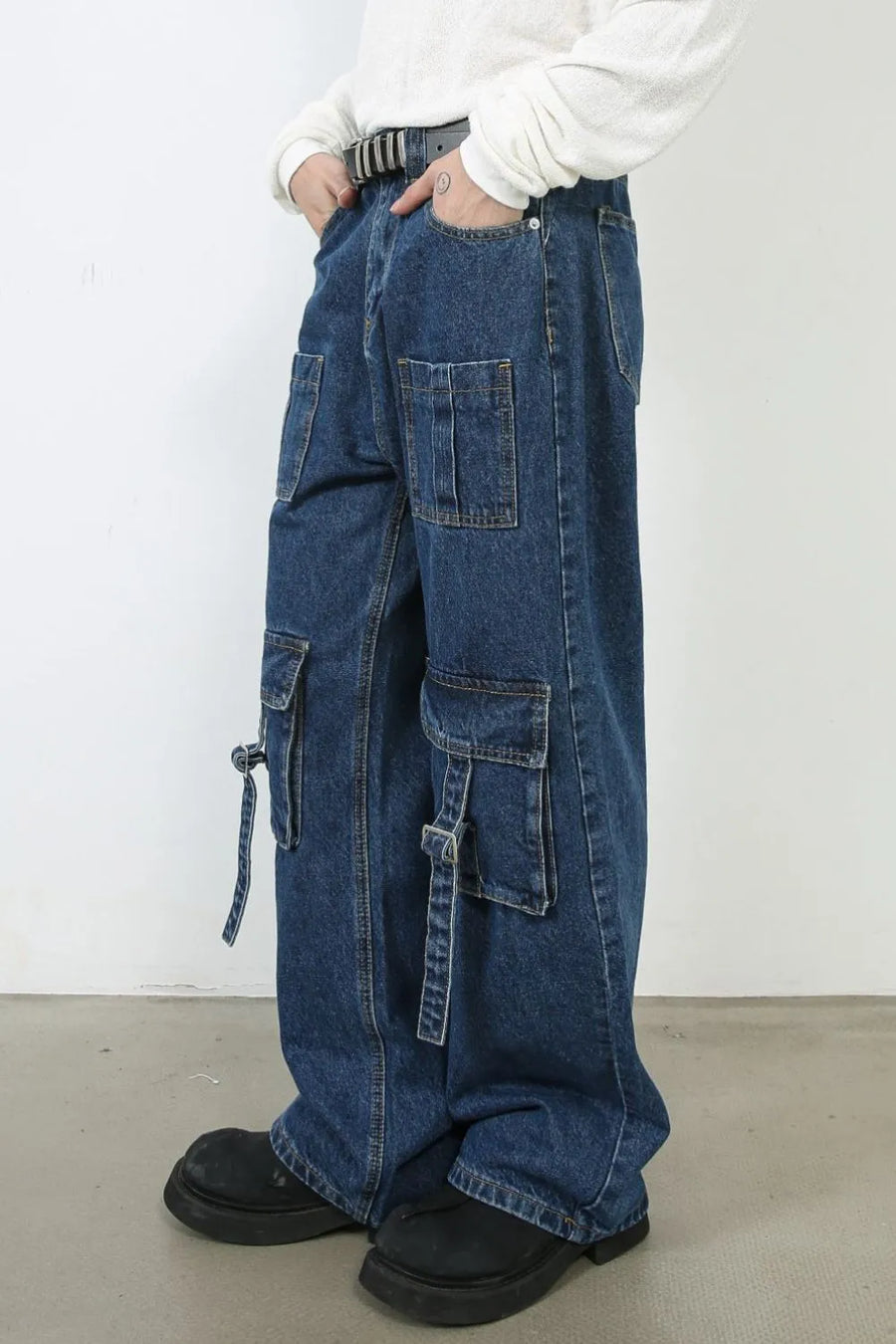 Medium wash denim cargo pants with buckle strap pockets and wide leg cut.