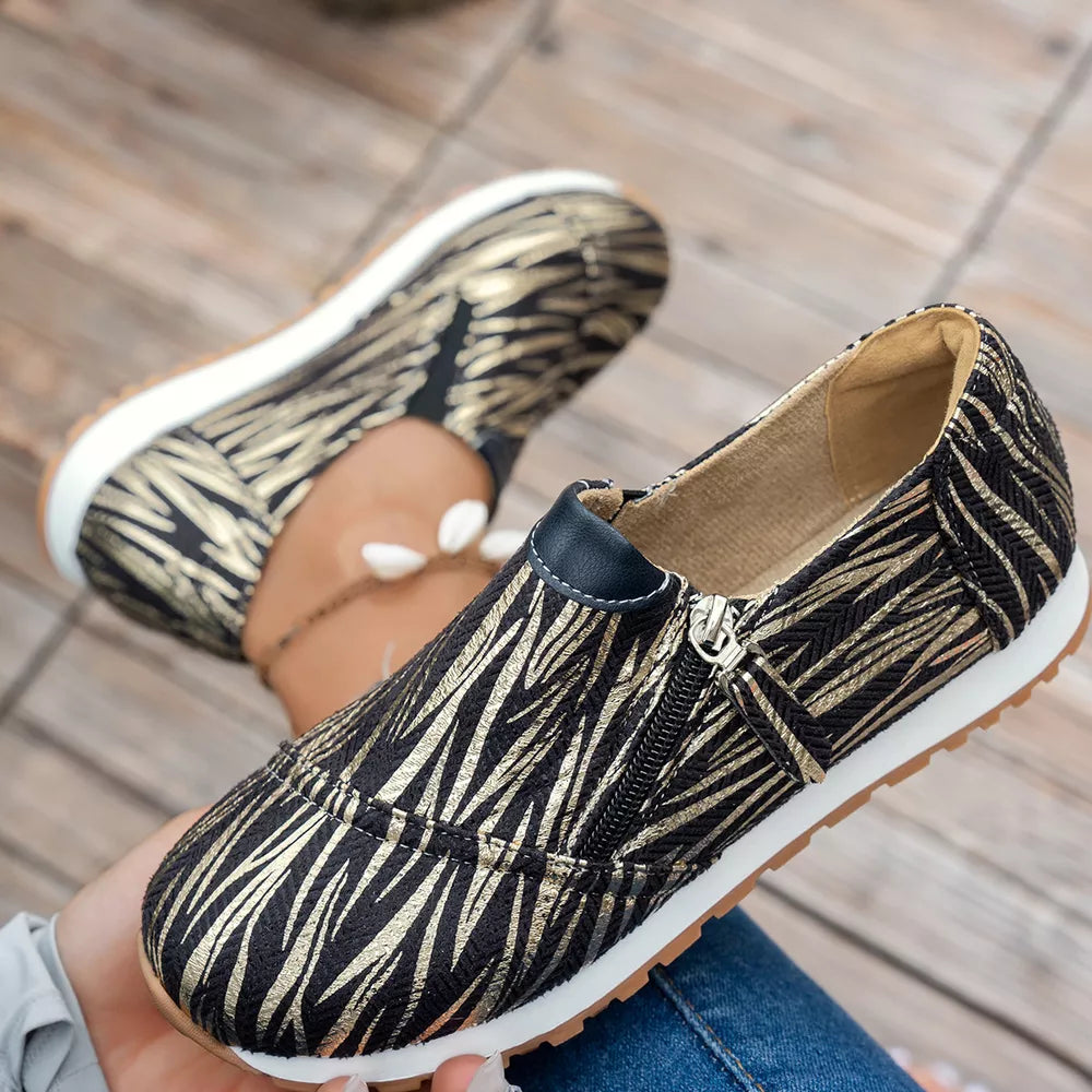 Zebra print slip-on flats with a side zipper detail in black and gold.