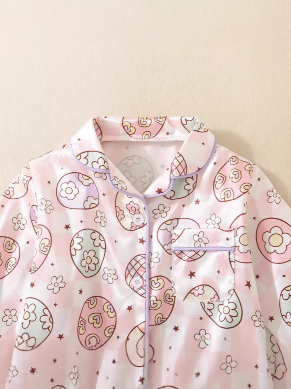 Toddler button-down pajama top with pink egg print, flowers, and stars on a pink checkered background.