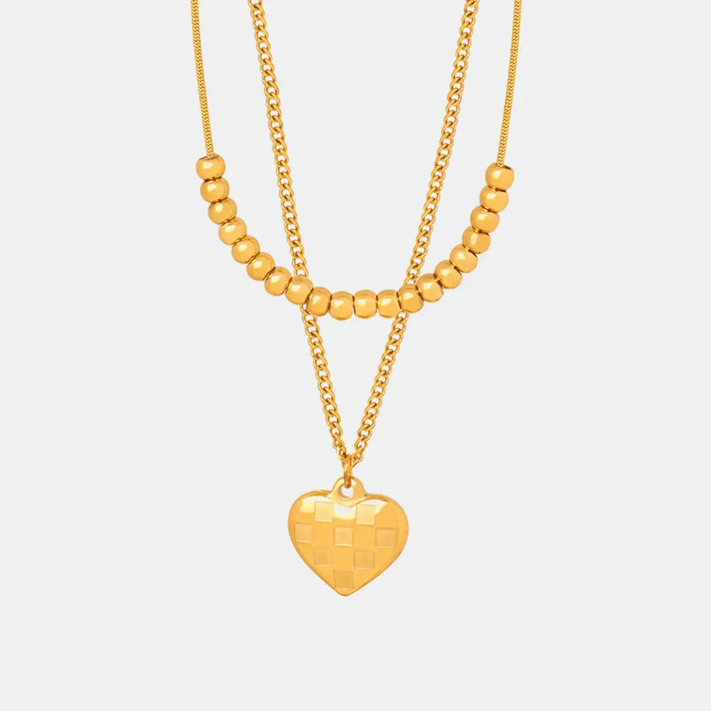 Gold layered necklace with beaded chains and a checkered heart charm.