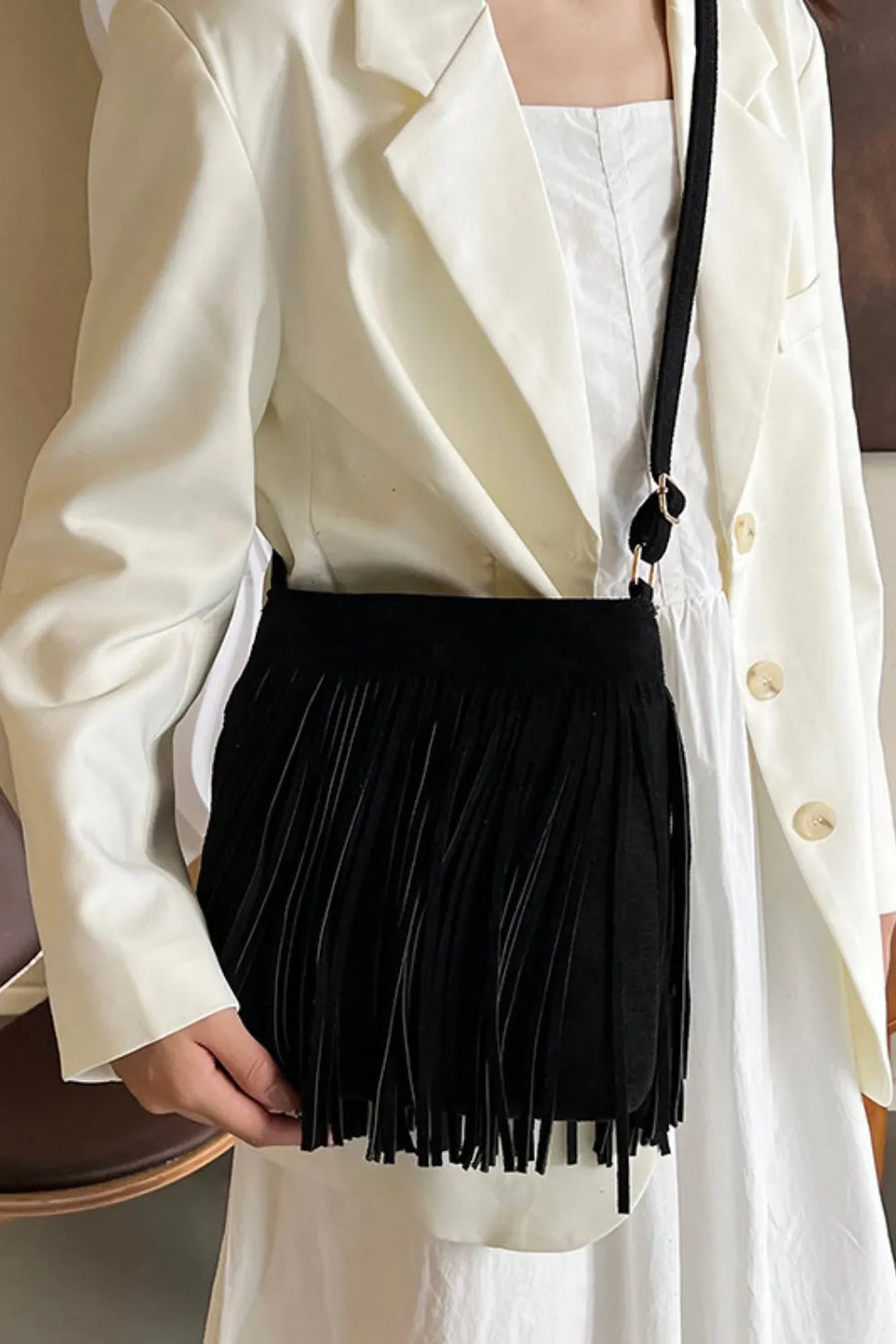 Black suede crossbody bag with fringe detail and adjustable strap.