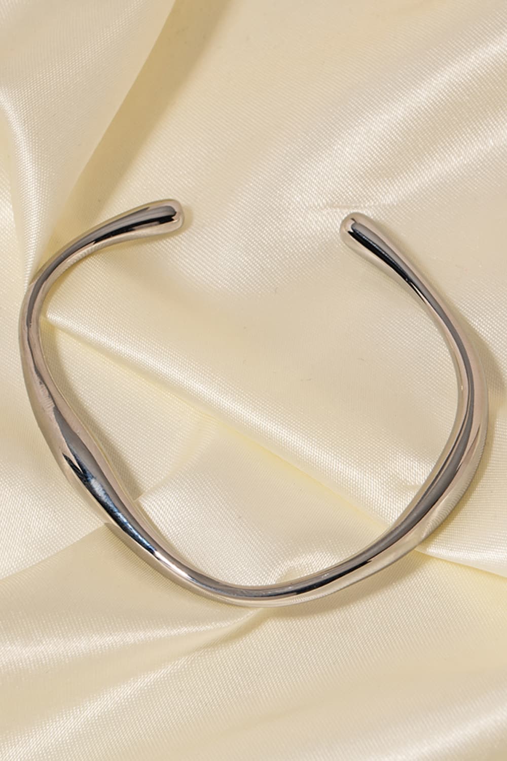 Sculpted silver open-ended bangle with a chic, fluid design on satin fabric.