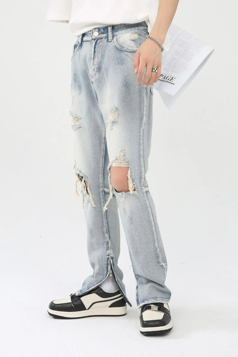 Light wash denim trousers with distressed knee slits and ankle zippers.
