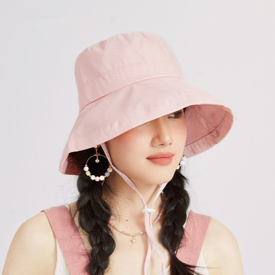 Pink striped bucket hat with wide brim and chin strap.
