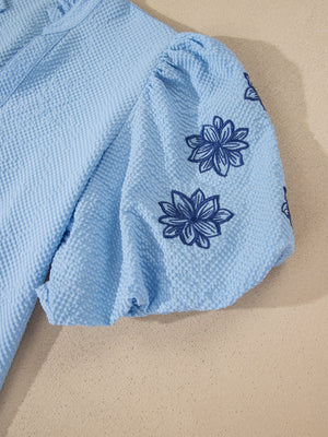 Light blue seersucker blouse with puff sleeves and dark blue floral embroidery.